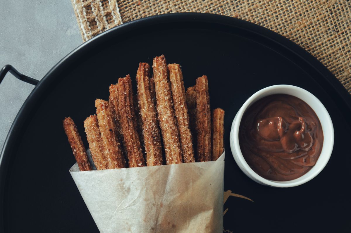 Tray of churros wrapped in paper with a bowl of chocolate sauce